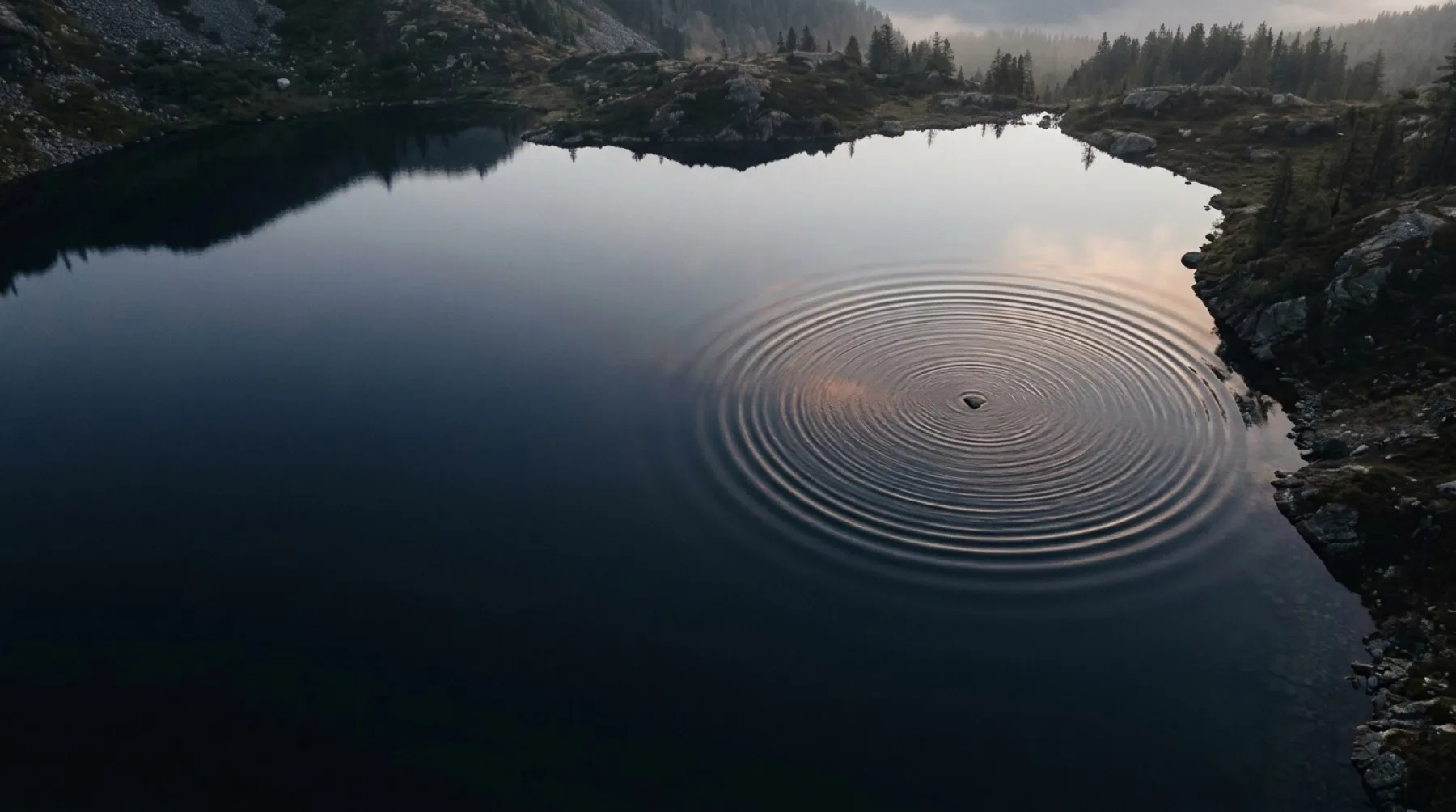Still mountain lake at dusk with rings spreading across dark water